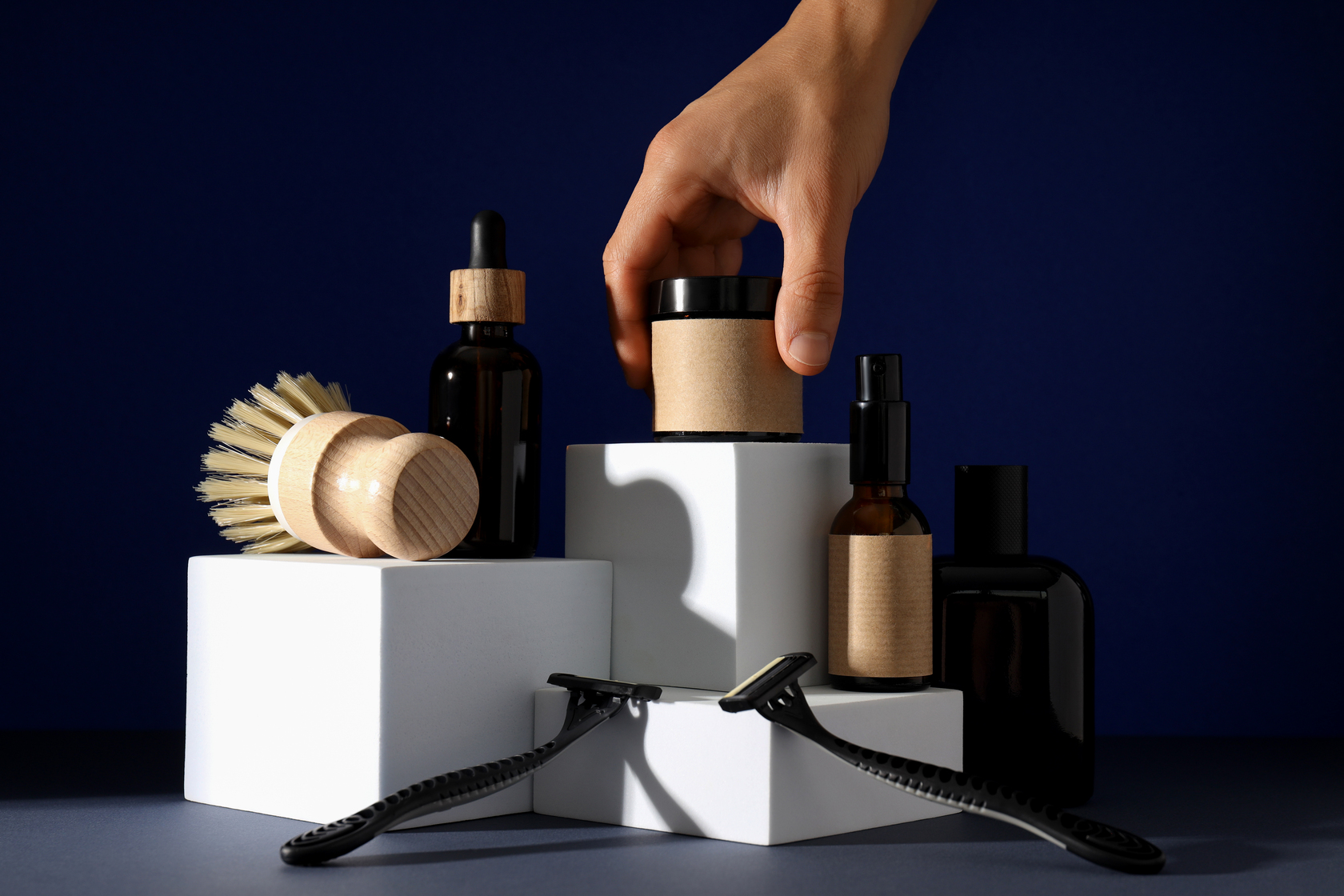 Shaving tools, bottles of men's cosmetics and hand on dark blue